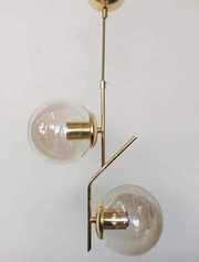 Lustra suspendata cu 2 globuri de sticla transparenta, structura metalica aurie, soclu E27, max 60W, design modern asimetric