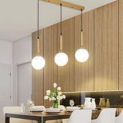 Lustra cu 3 pendule glob alb mat auriu, montata deasupra mesei de dining intr-un interior modern