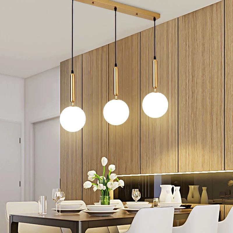 Lustra cu 3 pendule glob alb mat auriu, montata deasupra mesei de dining intr-un interior modern