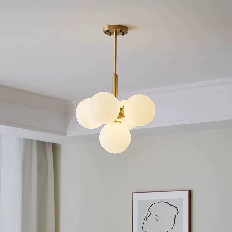 Lustra cu globuri sferice albe pe tija aurie, montata in living, aspect decorativ elegant