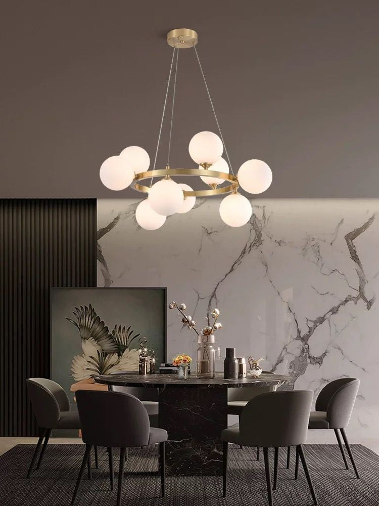 Lustra cu globuri albe si structura aurie montata deasupra mesei de dining intr-un interior modern