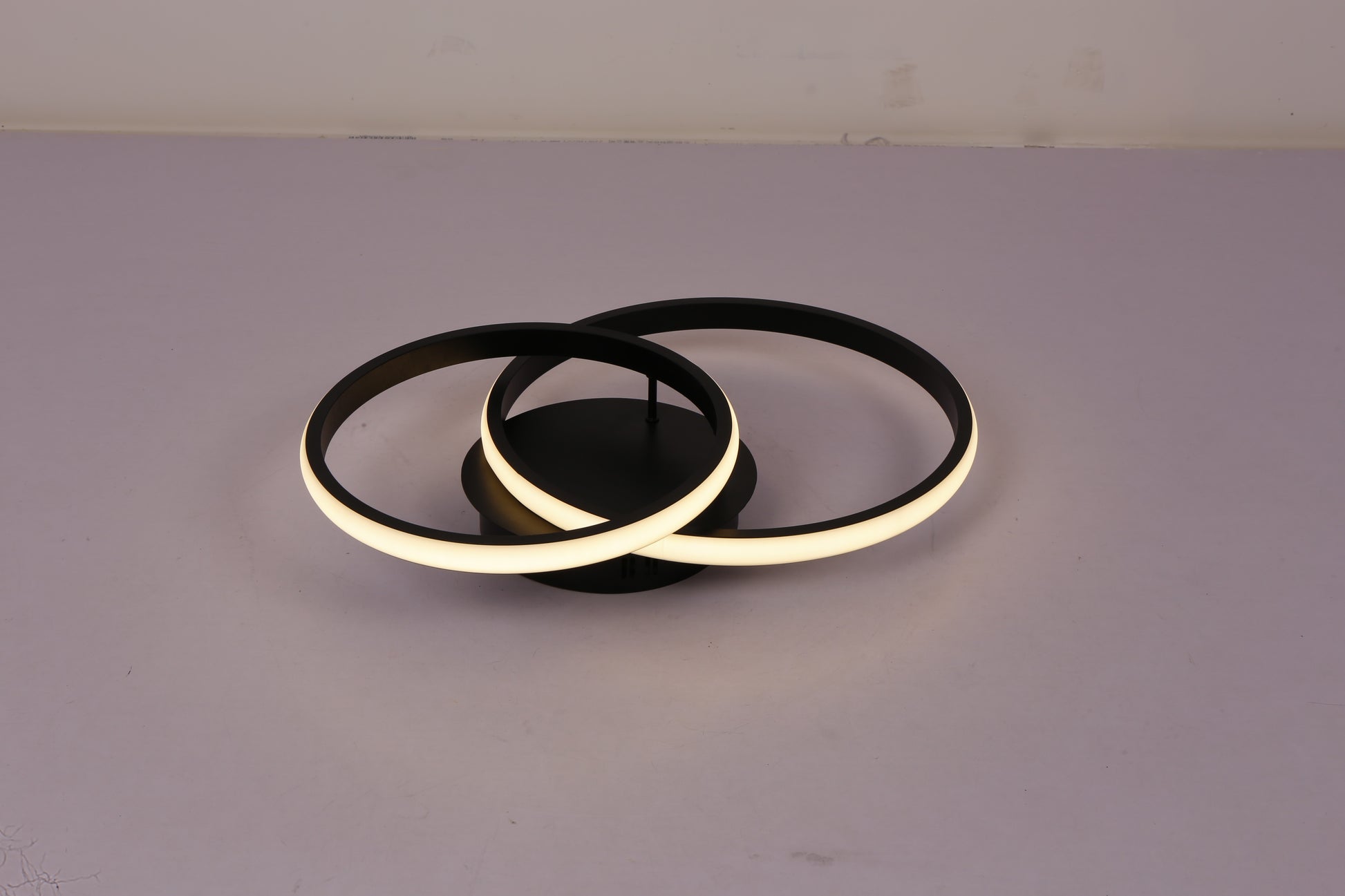 Plafoniera LED doua inele negre aprinsa, lumina calda intensa, vedere de sus pe fond gri
