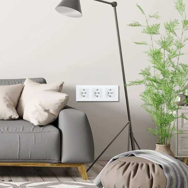 Priza tripla alba cu rama din sticla, montata in perete in living modern