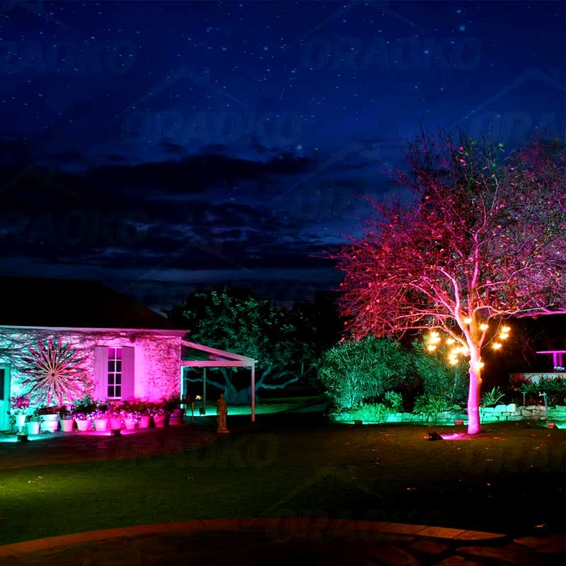Proiector LED RGB 50W iluminand o gradina si arbori noaptea in culori roz si verde, ambientare exterioara