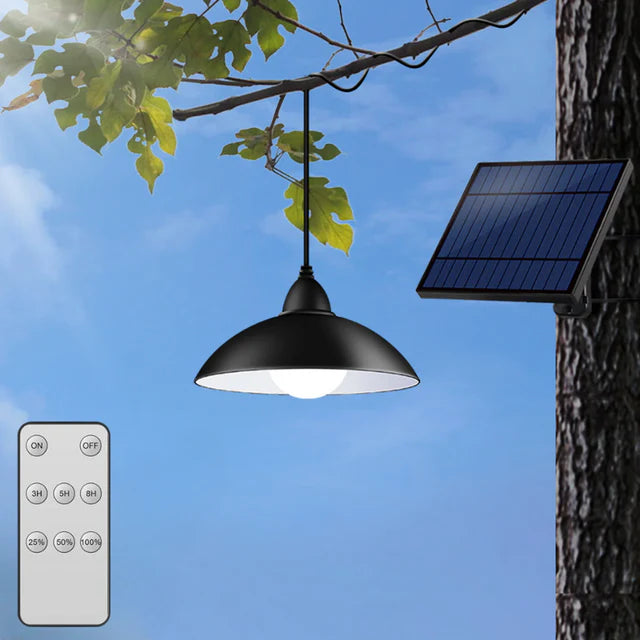 Candelabru solar agatat in copac in exterior, cu panou fotovoltaic montat pe perete si telecomanda